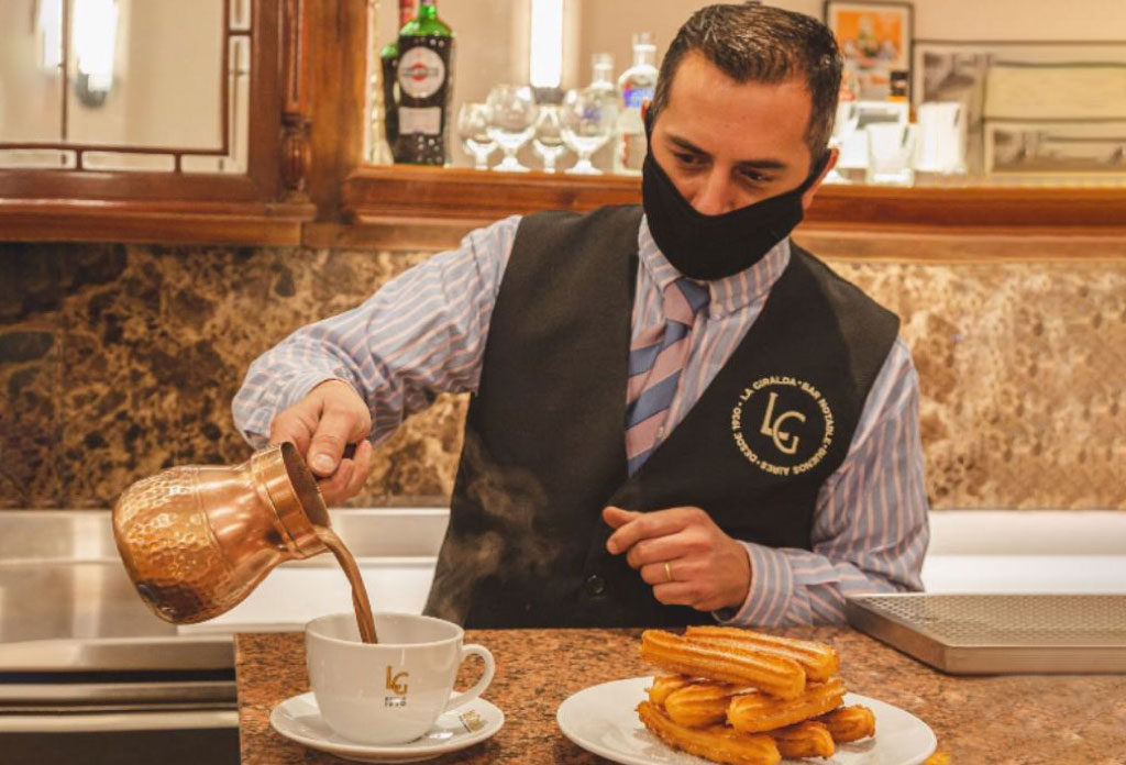 Un homme qui sert du chocolat chaud et un plat de churros dans le bar notable La Girlada à Buenos Aires.