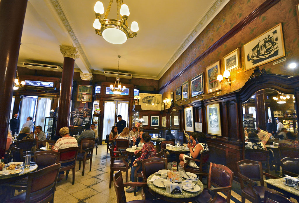 Intérieur du Café Tortoni à Buenos Aires. Plusieurs personnes sont assises pour manger et boire du café. Les murs sont décorés de boiseries.