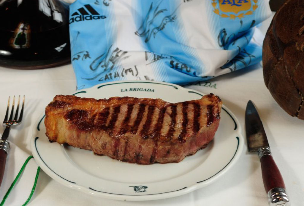 Dans une assiette avec des couverts sur les côtés. Derrière un maillot de football argentin. Il fait partie de la liste de 5 meilleurs restaurants de viande à Buenos Aires.