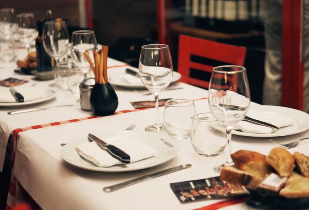 Salon du restaurant La Cabrera. Une longue table avec nappe, verres et paneras.
