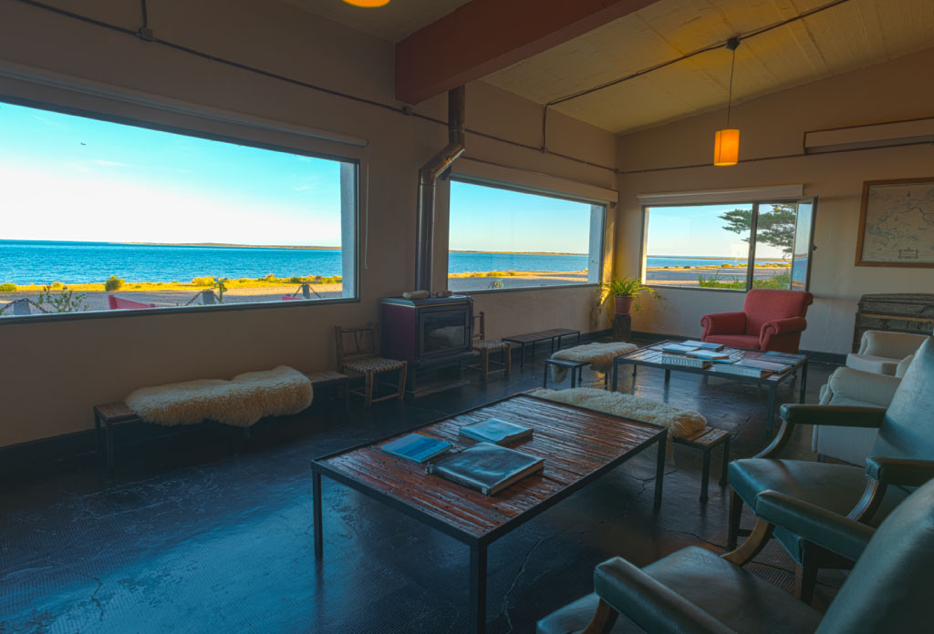 grand living avec une table basse, des feuteuilles et grandes fenêtres à l'océan
