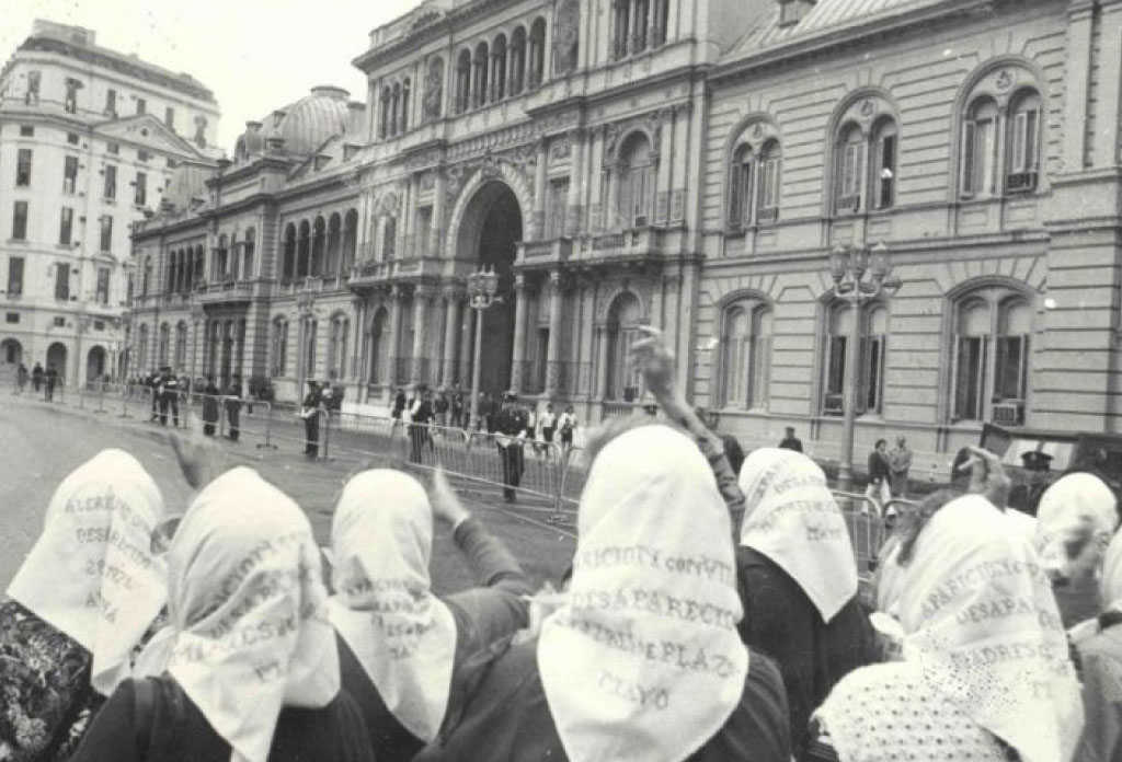 Des mères de la place de mai avec leurs foulards sur le dos observant la maison rose, siège du gouvernement en Argentine.