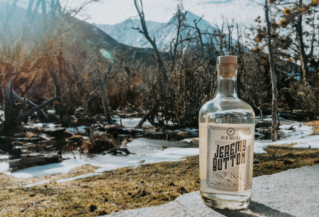 une bouteille de gin produit à Ushuaia et derrière un paysage d’arbres, de lacs et de montagnes
