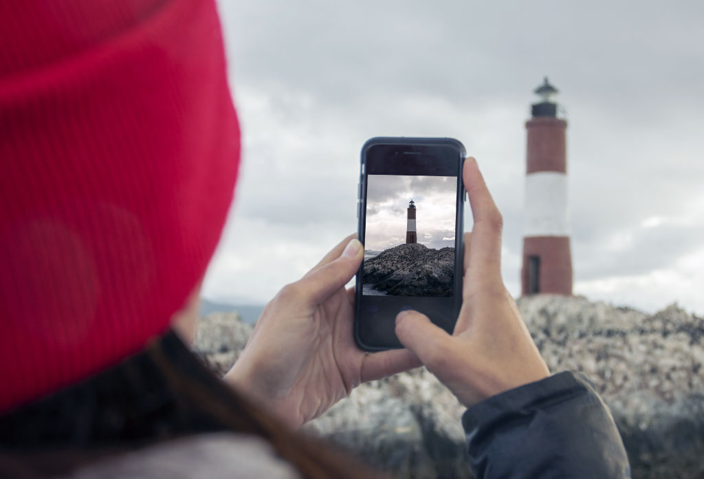 une femme tient un téléphone mobile en prenant la photo du phare Les Eclaireurs