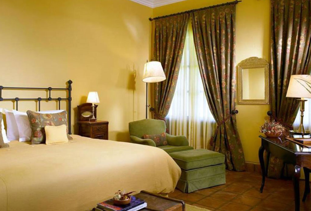 Chambre d’hôtel avec un lit double, fauteuil et lampe.