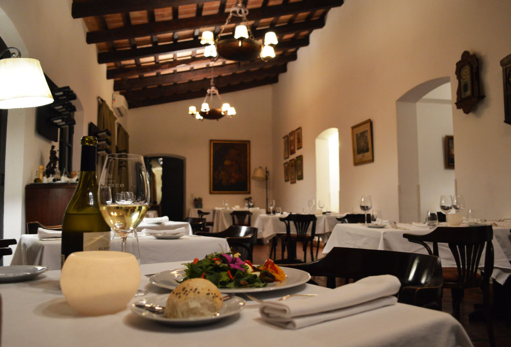 Restaurant de l’hôtel Patios de Cafayate. Plusieurs tables avec des plats servis et des bougies. Un verre de vin avec bouteille à côté.