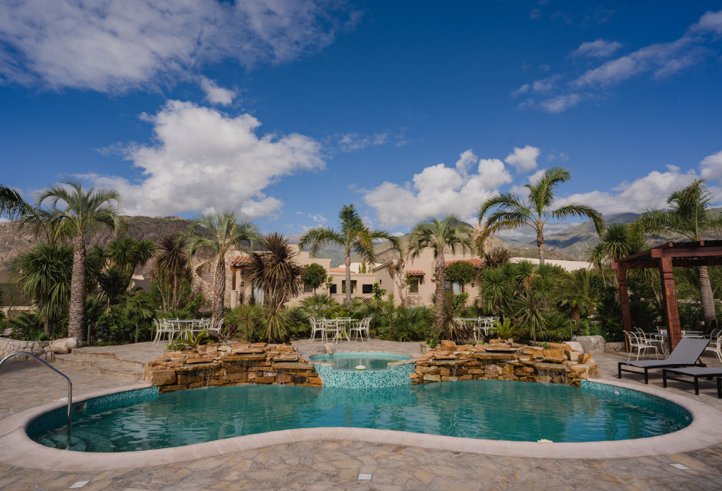 piscine de l’hôtel avec des palmiers de fond et des chambres