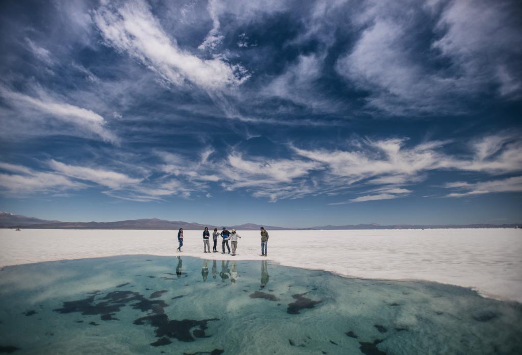 groupe de personnes debout sur un champ de sel et devant elles un petit lac