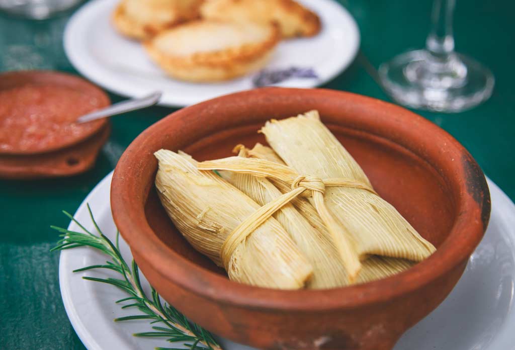 Table en bois vert et dessus des plats avec des repas typiques. Au premier plan un humita, plat typique de Salta et du nord-ouest argentin.