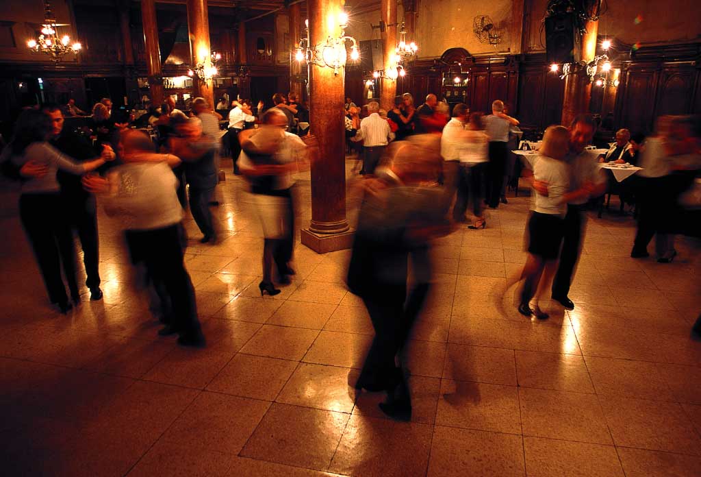 plusieurs personnes dansant le tango et se serrant l'une contre l'autre dans une salle avec des tables