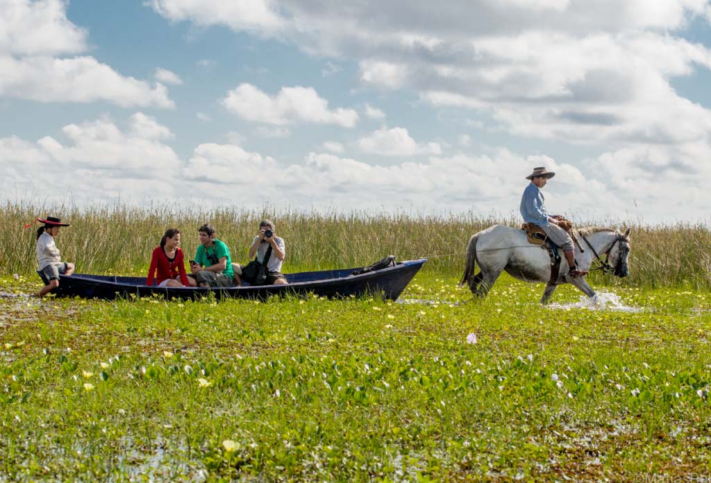 4 personnes dans un canoë et une autre sur un cheval au milieu d’un marais