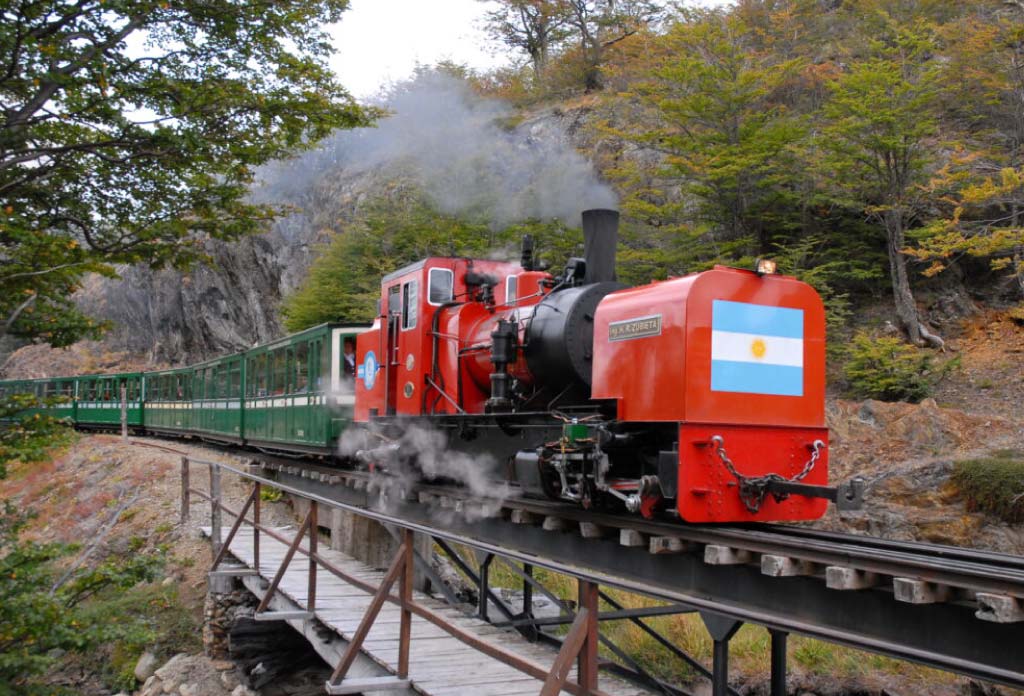 Une locomotive rouge avec des wagons Veres qui passent sur un pont. C’est le train du bout du monde.