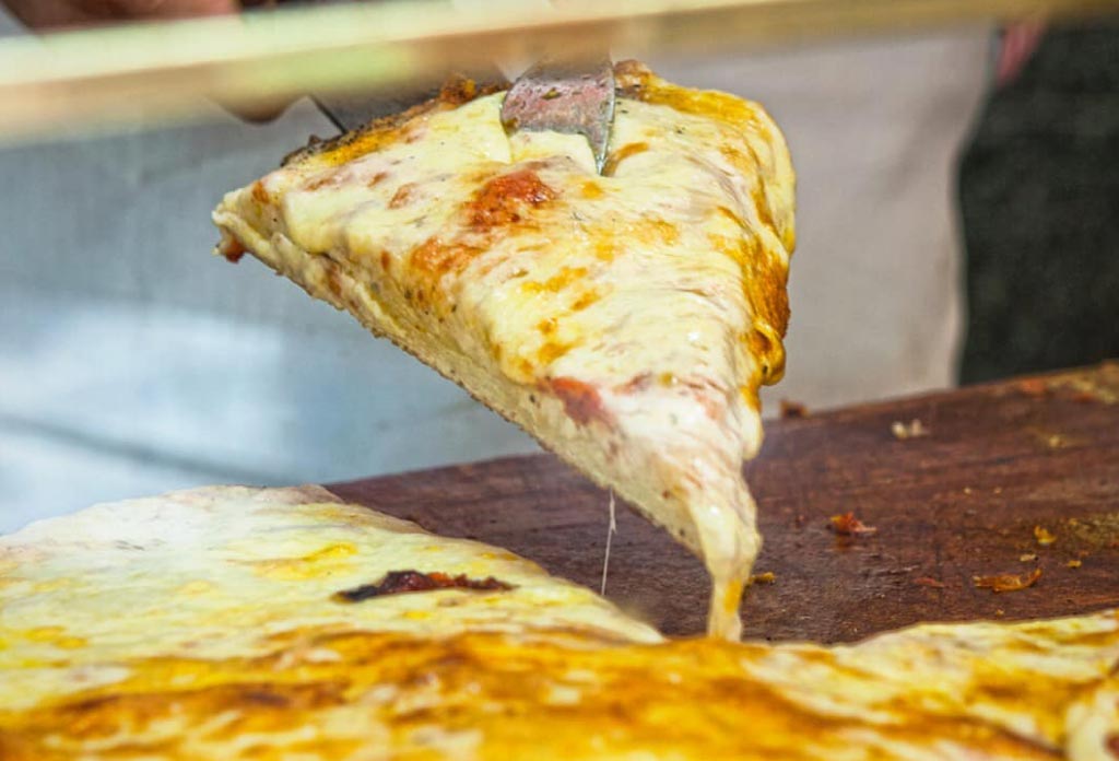 une main soulève une part de pizza et le fromage en tombe