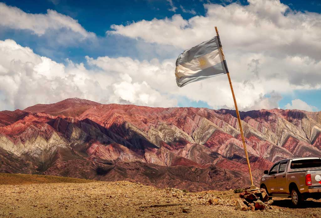 Montagne montagneuse du Hornocal avec beaucoup de couleurs, une camionnette et un mât avec drapeau argentin