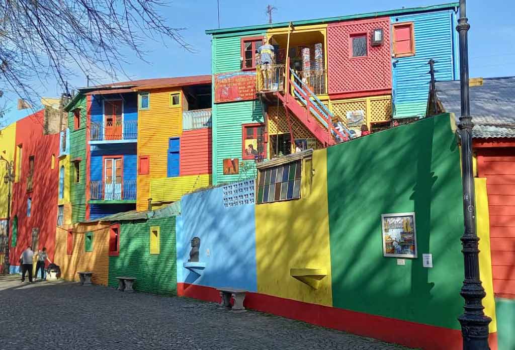 Une rue piétonne avec plusieurs maisons, dont les murs en tôle et en brique sont peints de couleurs.