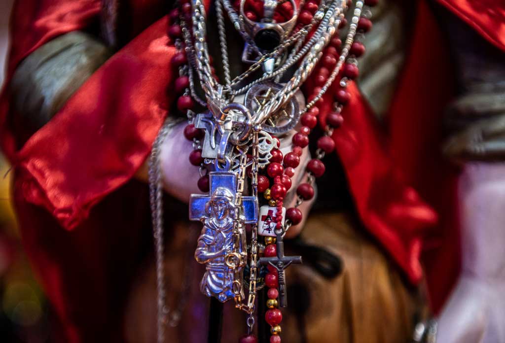 une sculpture du Gauchito Gil tenant un chapelet, une étoile de david, colliers et bijoux