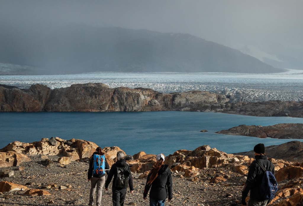 groupe de personnes marchant devant un lac avec un glacier