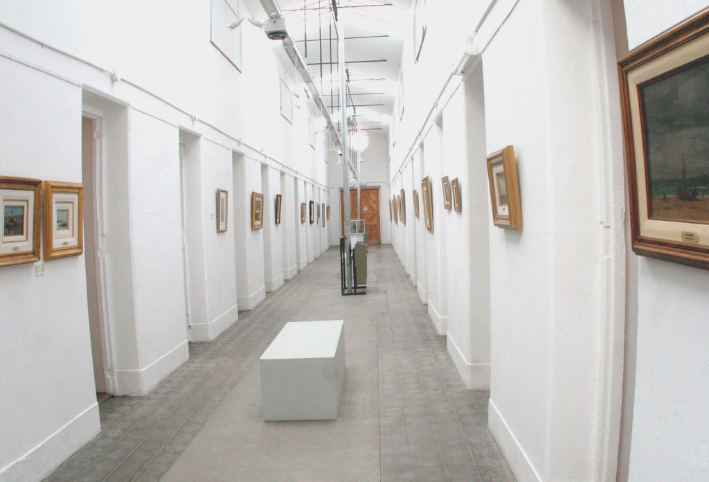 Ancien couloir de la prison d'Ushuaia aujourd'hui transformé en salle d'art avec des tableaux accrochés.
