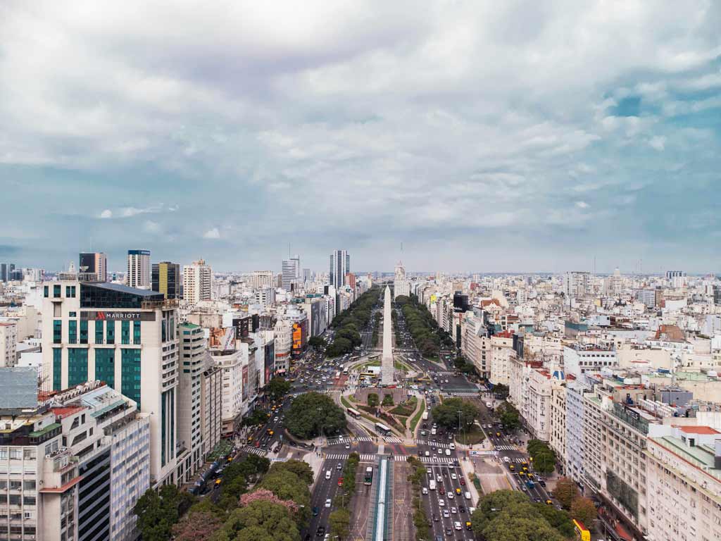 photo aérienne de l’avenue 9 de Julio et de l’obélisque de Buenos Aires. Sur les côtés de l’avenue il y a des bâtiments.